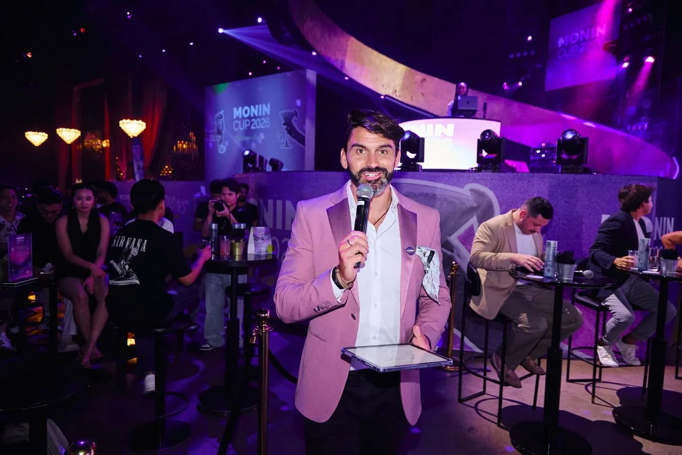 Darryl Rees hosting the Monin Cup 2026 with a microphone and tablet in Dubai