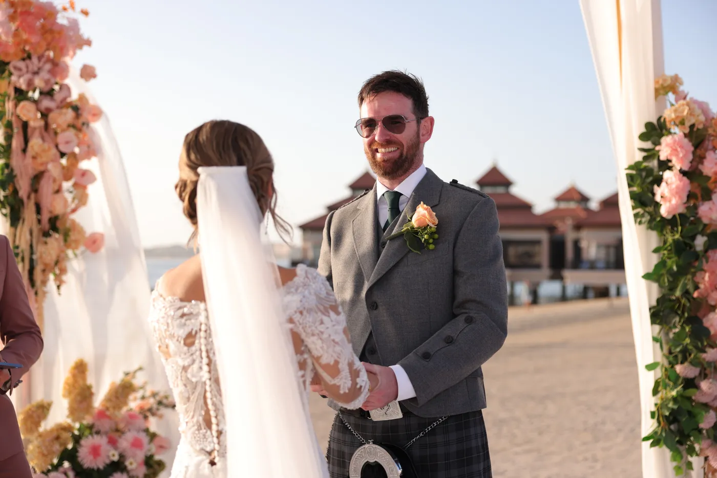 Bride and groom holding hands under a floral arch at their Dubai beach wedding