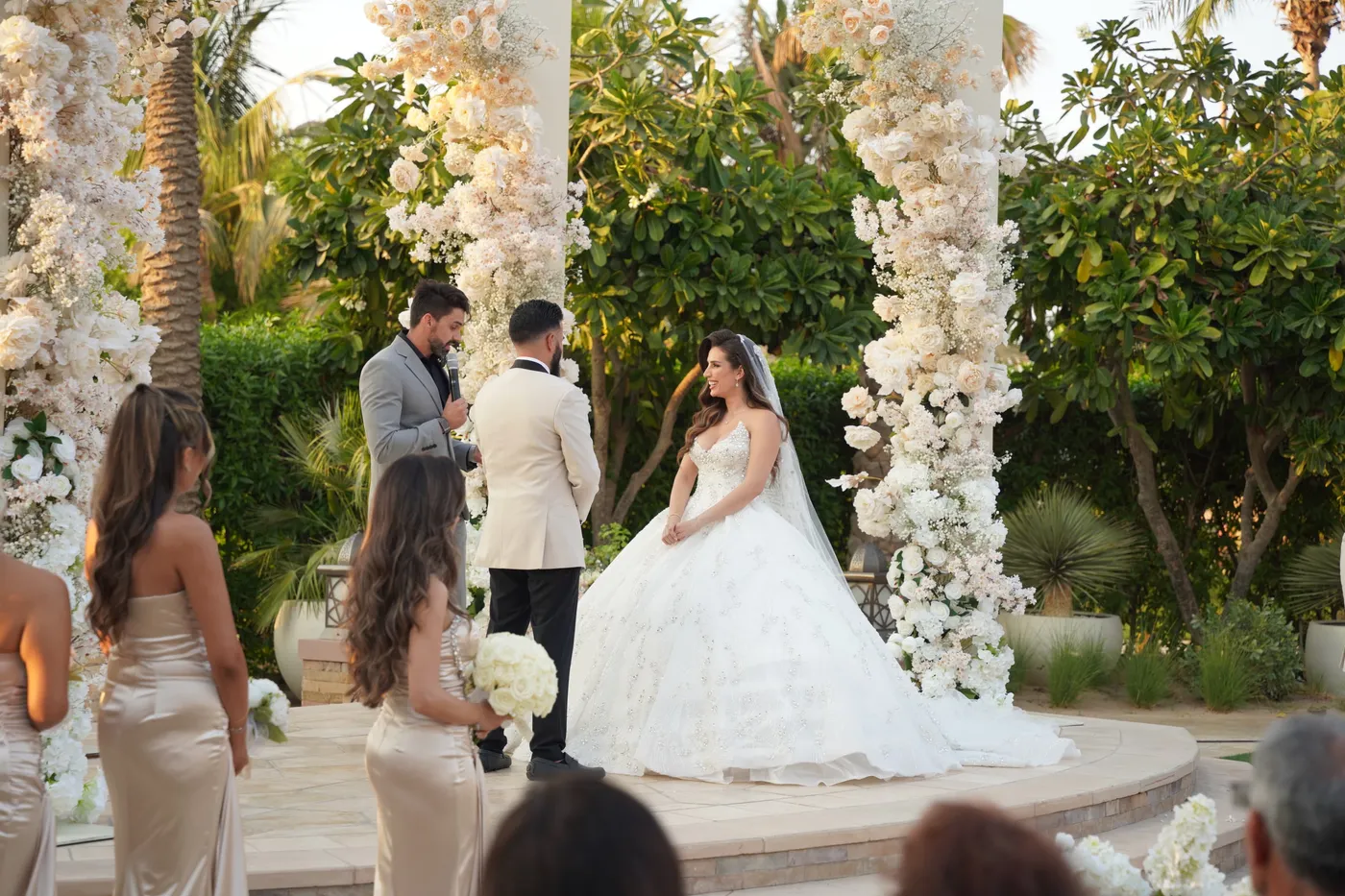 Darryl Rees officiating a garden wedding ceremony under a white floral arch in Dubai