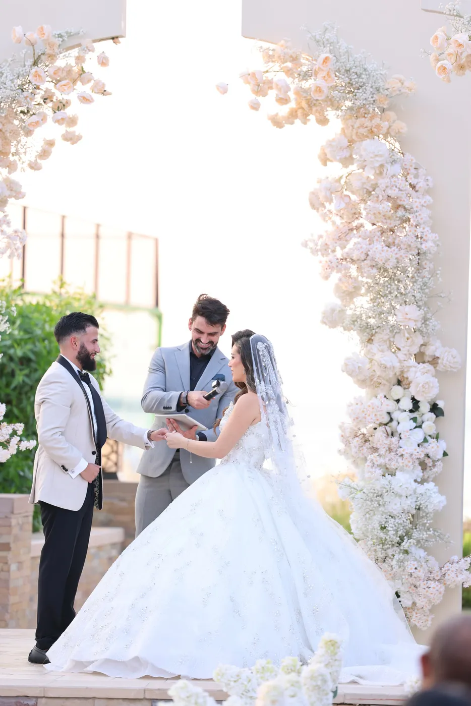 Darryl Rees officiating a ceremony for a bride and groom under a floral arch