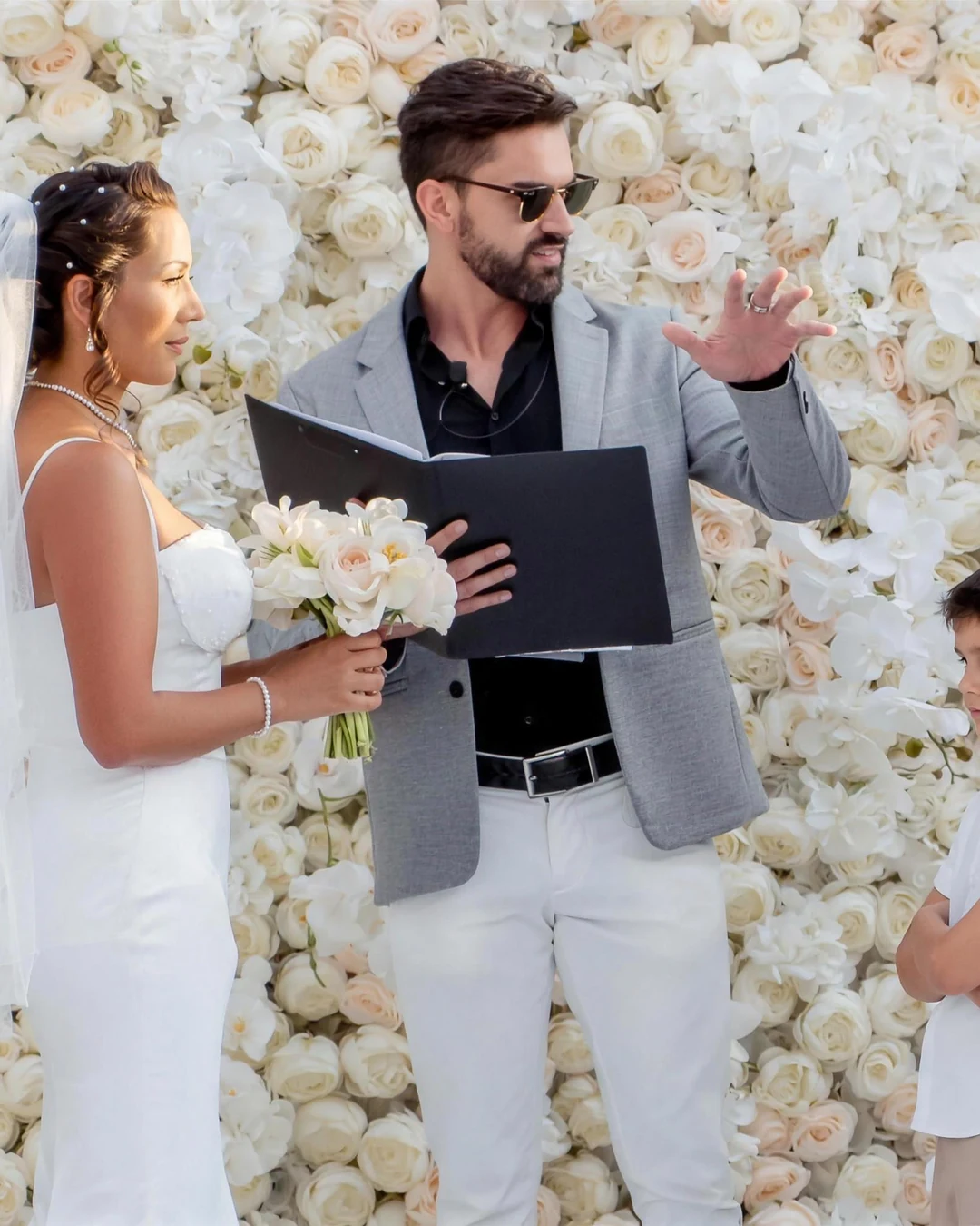 Darryl Rees leading a wedding ceremony in front of a white flower wall in Dubai
